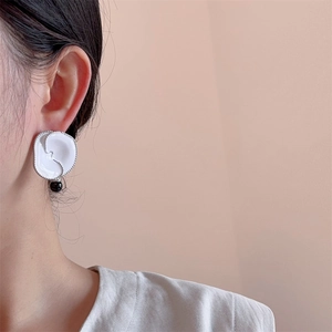 Detail of white enamel flower earring with black pearl drop on a model ear