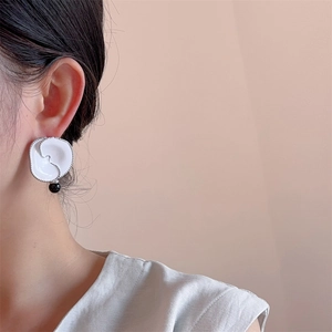Elegant wave-shaped white enamel earrings with black onyx bead on a female model