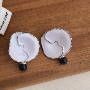 Detailed view of white enamel flower earrings with black beads on a wooden background