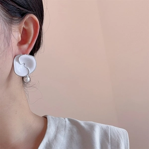 Close-up of white enamel flower earring with pearl drop on a female ear