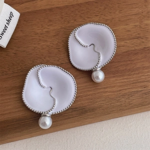 Detail of white enamel flower earring with silver beads and hanging pearl on wood