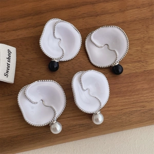 Elegant white enamel and black onyx pearl flower earrings on a dark walnut wood background