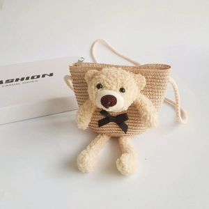 Detailed view of cream straw crossbody bag featuring a plush teddy bear with black bow