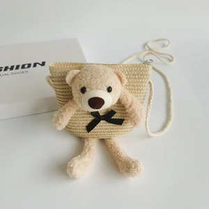 Detail of beige woven straw kids bag featuring a cute plush bear with a black bow