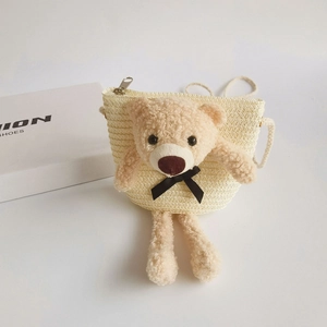 Detail of a beige straw crossbody bag featuring a 3D plush bear and metal zipper