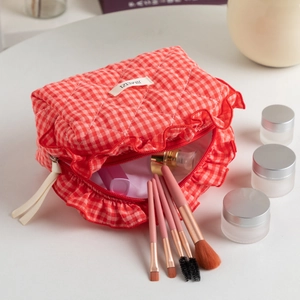 Close-up of red checkered quilted makeup bag with ruffle trim and beauty essentials