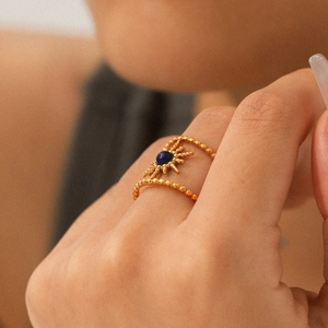 Gold double beaded ring with sunburst charm and blue gemstone on a finger