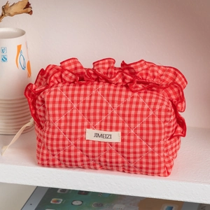 Detail of red gingham quilted makeup bag featuring decorative ruffle edges and zipper