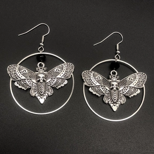 Gothic silver moth skull earrings with black beads on a minimalist dark background
