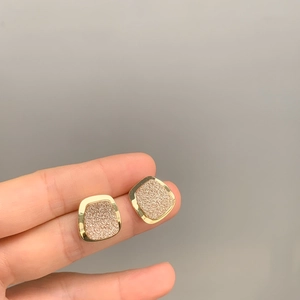 Dettaglio di orecchini quadrati dorati con trama glitterata rosa opaca in mano