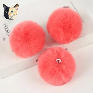 Three coral pink faux rabbit fur pom poms with hanging loops on a decorative white book