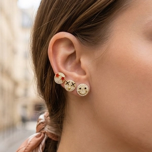 Close-up of 18K gold smiley face earrings set with sparkling zircon on a model's ear
