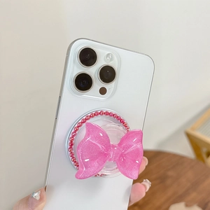 Detail view of pink glitter bow MagSafe phone grip with beaded base on white smartphone