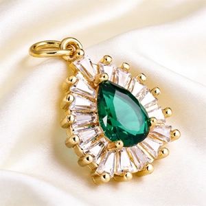Macro view of teardrop emerald crystal pendant with baguette zircon halo on silk