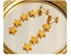 Vue macro de boucles d'oreilles étoiles pendantes en acier plaqué or 18k sur miroir