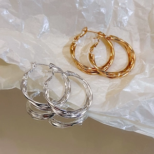 Detailed close-up of layered twisted silver and gold hoop earrings on a reflective surface