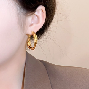 Close-up of elegant gold twisted hoop earrings worn by a model in a brown blazer