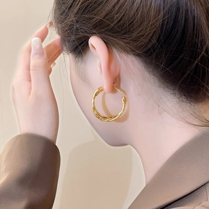 Macro detail of large gold multi-layer twisted hoop earrings on model with glossy finish