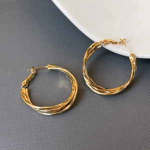 Macro detail of gold twisted hoop earrings showing intricate multilayer braided texture