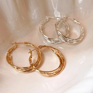 Detailed view of intertwined gold and silver textured hoop earrings on white ceramic