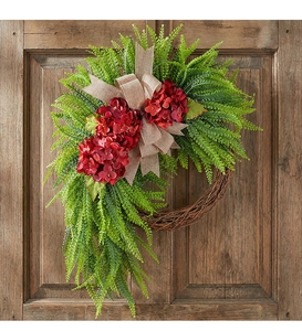 Close-up of artificial hydrangea wreath with ferns and linen bow on a wooden door