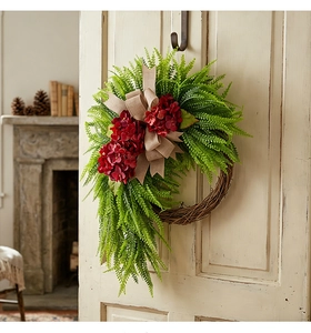 Close-up of artificial hydrangea wreath with green ferns and rustic burlap bow on wooden door