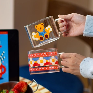 Detail view of transparent glass mugs with colorful bear and flower prints and handles