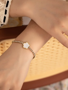Détail du bracelet trèfle doré avec cristaux sur manche élégante en dentelle blanche