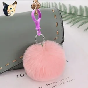 Close-up of a pink faux fur pompom with purple clip on a gray leather bag