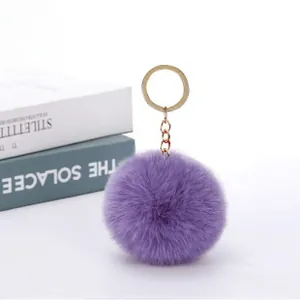 Close-up of fluffy dark purple faux rabbit fur pompom with golden metal keychain ring