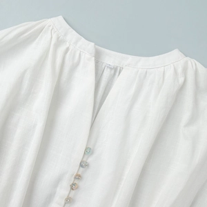 Detail of white cotton top featuring V-neckline with shell buttons and pleat textures