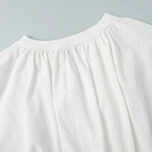 Detail of white cotton blouse showing round neck with pleated fabric texture and stitching