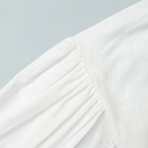 Detail shot of pleated shoulder seam on a white cotton blouse with natural fabric texture