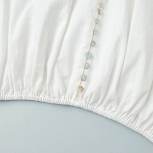 Detail of white cotton top with colorful shell buttons and elastic gathered hemline