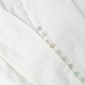 Macro detail of the white cotton V-neckline featuring elegant iridescent shell buttons