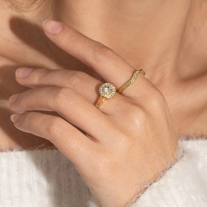 Elegant gold-tone halo engagement ring set with wavy diamond bands worn on a hand