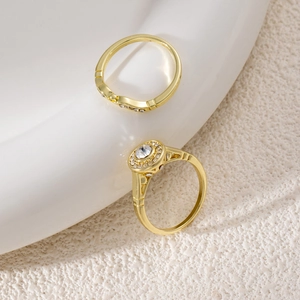 Detail of two gold-plated rings featuring white zircon stones on a minimalist texture