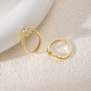Detail view of two gold-plated rings with round-cut zircon stones on a stone surface