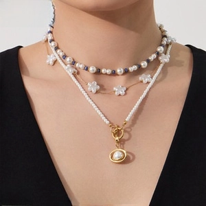 Detailed close-up of a three-layer pearl necklace set with a floral pendant on a model