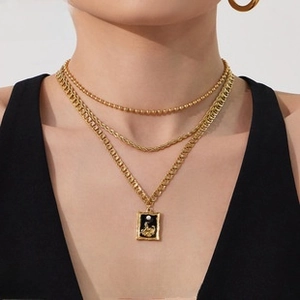 Detailed view of layered gold necklaces with black pendant on model in black outfit