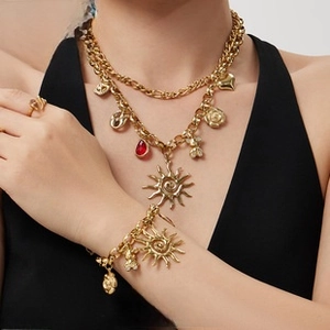 Detail of gold layered necklace set with heart and sun charms on a model vest