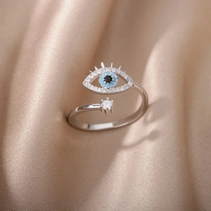 Silver evil eye open ring with blue and black gems on champagne satin background