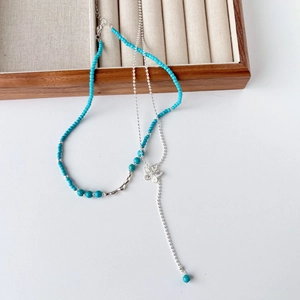 Double layered turquoise beaded necklace with butterfly pendant on wooden jewelry display