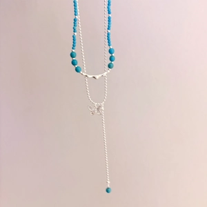 Macro detail of a layered necklace with blue beads and a hollow butterfly pendant