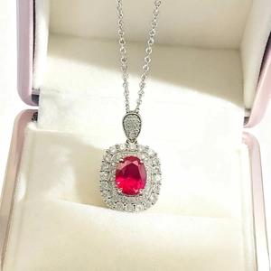 Close-up of a luxury oval red gemstone pendant with double halo white diamonds in a gift box