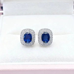 Detailed close-up of oval sapphire halo earrings with micro-paved diamonds in a gift box