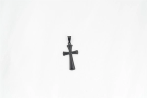 Détail d'un pendentif croix noir mat avec des bords perlés texturés et un centre lisse