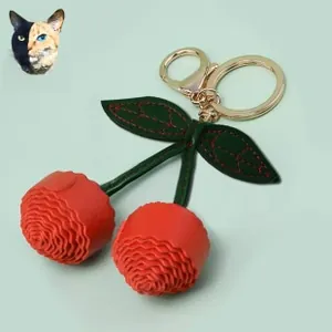 Detail view of handmade red leather double cherry keychain with green leaves and gold hardware