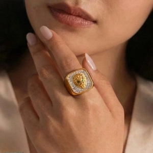 Close-up of golden lion head square ring with green gem eyes and pavé stones