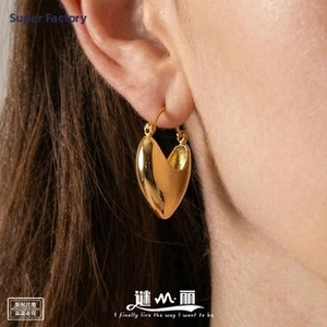 Close-up of polished golden heart-shaped stud earring worn by a model in a minimalist style